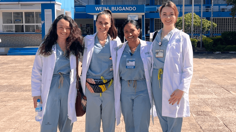 Four women in scrubs and white coats, standing outside a hospital building.